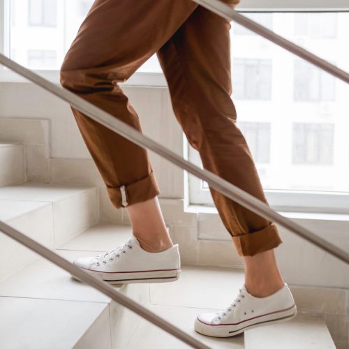 Woman,In,White,Sneakers,And,Khaki,Trousers,Goes,Upstairs,To